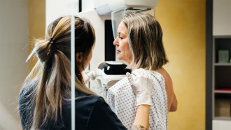 Woman in a hospital gown getting a mammography with the help of a health care worker.