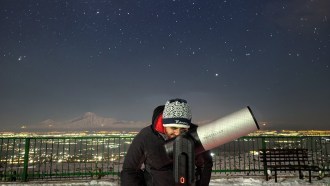 A person looks through a telescope at the night sky.