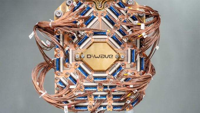 A piece of computer hardware shows a lot of wires surrounding a D-Wave logo.
