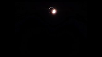 A bright burst of light shines from the edge of a dark disk, creating a dramatic contrast against the black sky.