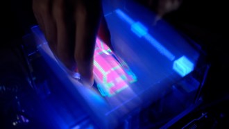 a hand reaches down into an illuminated screen displaying a 3-D graphic of a car