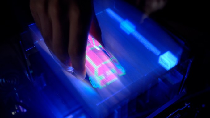 a hand reaches down into an illuminated screen displaying a 3-D graphic of a car